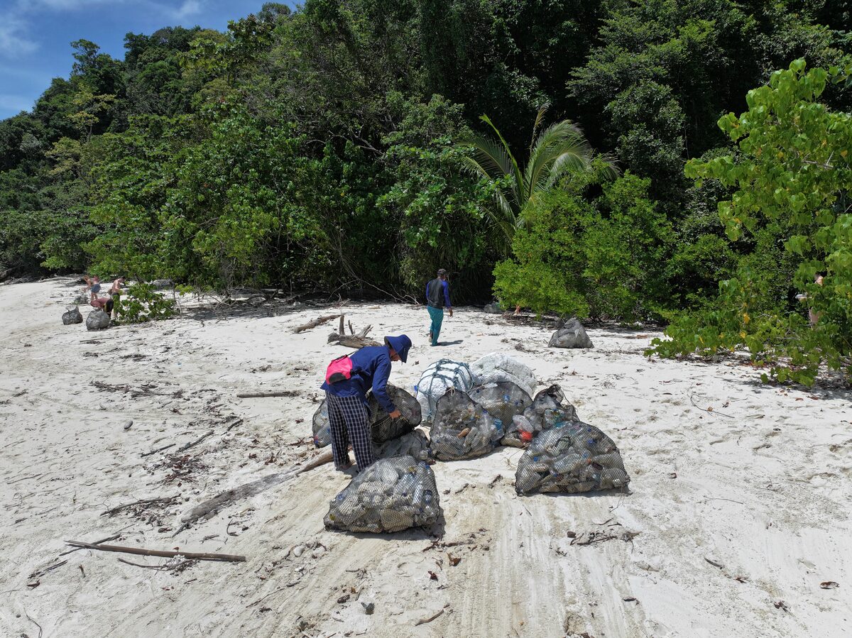 Eine Person bindet volle Müllsäcke im Sand am Rand des Dschungels zu.